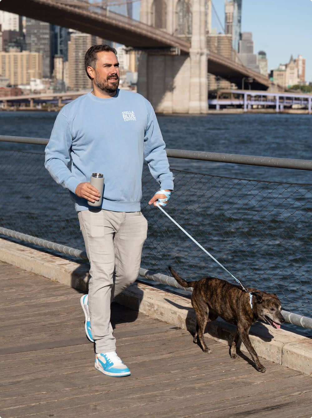 Big Kat on a boardwalk holding a leash for Stella Blue with a thermos in his hand